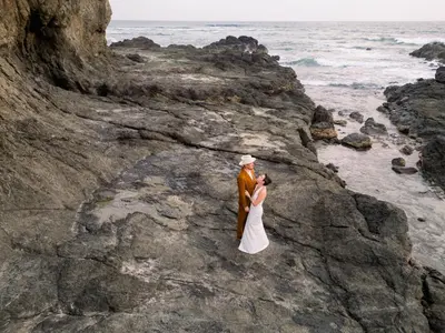 a bride and groom standing on a rock by the ocean at Boutique Surf Hotel Rip Jack Inn in Playa Grande