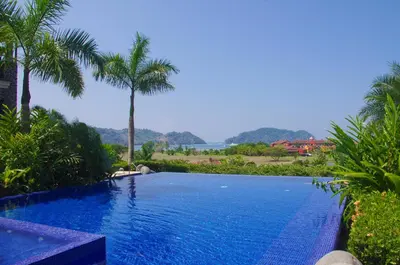 a swimming pool in a resort with palm trees at Vista Bahia 1F 1 bdr Ocean View in Los Suenos in Herradura
