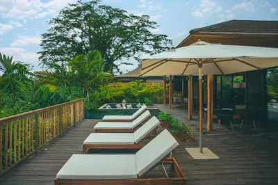 a deck with benches and an umbrella and a pool at Nayara Tented Camp in Fortuna