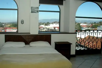 a bedroom with a bed and two windows at Alajuela Backpackers Airport Hostel in Alajuela City