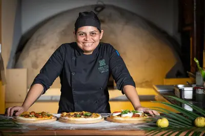 a woman standing in a kitchen with three pizzas at Buena Vista del Rincón Eco Adventure Park Hotel & Spa in Liberia