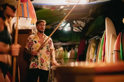 a man in a hawaiian shirt standing in front of surfboards at El Gato Rojas Surf Hostel in Santa Teresa Beach