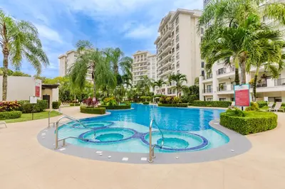 a large swimming pool with palm trees and buildings at Apt AC WIFI Mountain View Near beach Costa Rica in Jacó