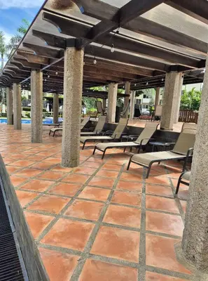 a patio with lounge chairs under a wooden roof at Family getaway, pool, beach and surf in Jacó