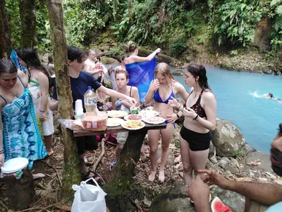 a group of people standing around a picnic table by a river at Posada Río Celeste La Amistad in Rio Celeste