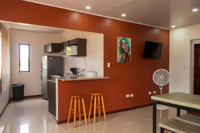 a kitchen with a bar with stools and a refrigerator at Aptos Casa Caribe, habitaciones privadas en aptos compartidos & aptos completos con auto entrada in Puerto Limón