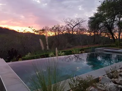a swimming pool in a garden with a sunset in the background at Baliyana Lodge in San José Pinilla