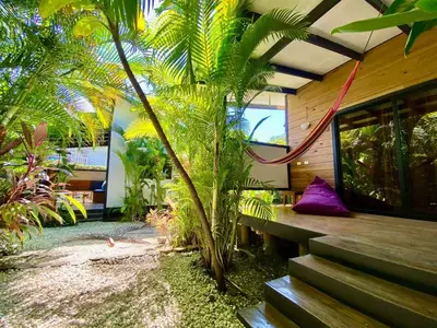 a house with a porch with a bench and palm trees at Santeria Lodge in Santa Teresa Beach