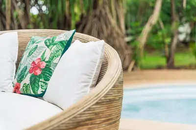 a wicker chair with white pillows sitting next to a pool at SoulShine in Playa Avellana