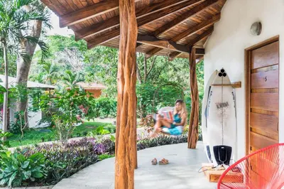 a woman sitting on the porch of a house with a surfboard at SoulShine in Playa Avellana