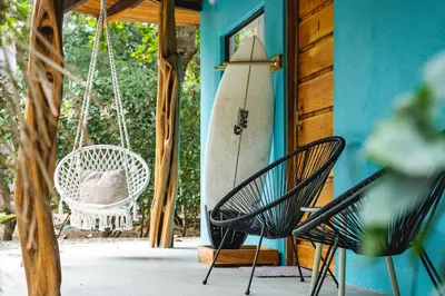 a porch with a swing and a surfboard on a house at SoulShine in Playa Avellana