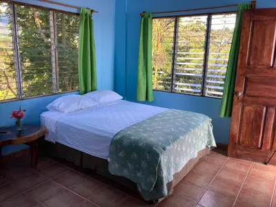 a bedroom with a bed with blue walls and windows at El Paraiso Azul in Ojochal