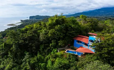 a blue house on a hill next to the ocean at El Paraiso Azul in Ojochal