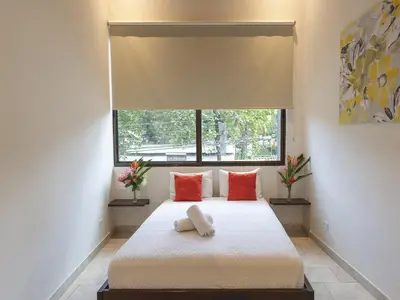 a bedroom with a bed with red pillows and a window at Surfside Apartments - Playa Carmen in Santa Teresa Beach