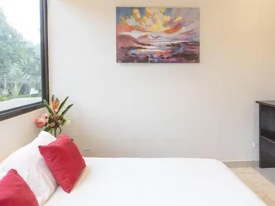 a white bed with red pillows and a painting on the wall at Surfside Apartments - Playa Carmen in Santa Teresa Beach