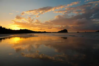 a sunset on a beach with the reflection in the water at Hotel Arboleda in Quepos
