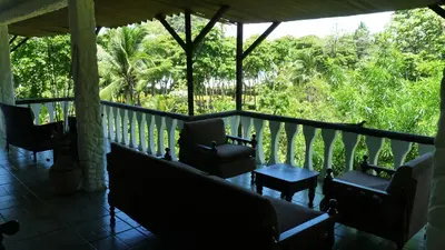 a porch with chairs and a table and trees at Hotel Arboleda in Quepos