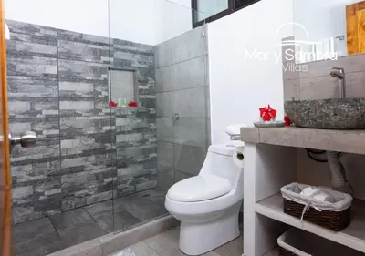 a bathroom with a toilet and a glass shower at Mar y Sombra Villas in Quepos