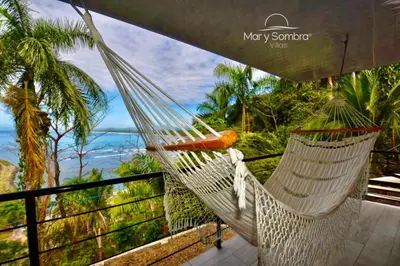 a hammock on a balcony with a view of the ocean at Mar y Sombra Villas in Quepos