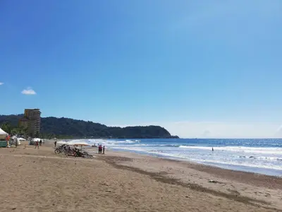 a beach with people on the sand and the ocean at 3Room Penthouse Beach Condo in Jacó