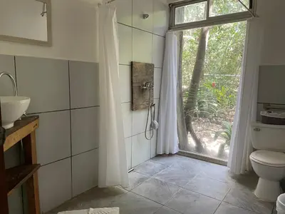 a bathroom with a shower and a toilet and a window at Nahele Lodge in Santa Teresa Beach