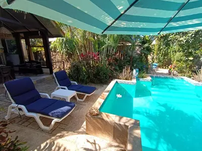 a swimming pool with two chairs and an umbrella at Suite Paraiso Azul in Tamarindo