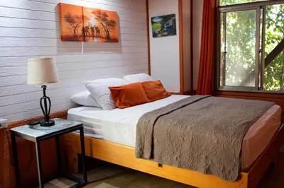a bedroom with a bed and a table with a lamp at Coyote Rooms in Cabuya