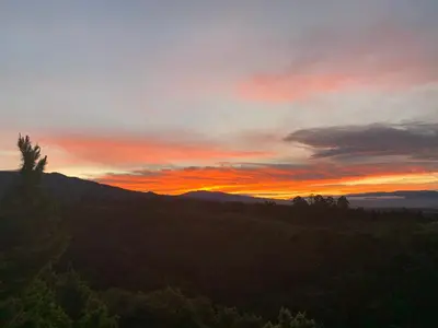 a sunset in the mountains with trees in the foreground at La Cabaña Poas in Poás