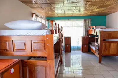a room with two bunk beds and a kitchen with a window at Hostel Bouganvilia Bed and Breakfast in San Ramón