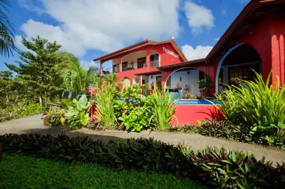 a red house with a garden in front of it at Toucan Lane in Nuevo Arenal