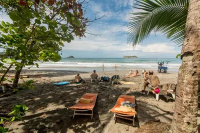 a group of people sitting in the sand on a beach at Karahe Beach Hotel in Manuel Antonio