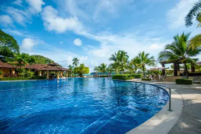 a swimming pool at a resort with palm trees at Marbella 1E 3 bdr Ocean View in Los Suenos in Herradura