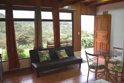 a living room with a couch and a table and windows at Monteluna Studios Monteverde in Monteverde Costa Rica