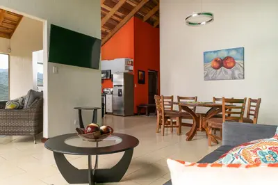 a living room with a table and a kitchen at Casa Sofia, a Gem Close to Orosi Thermal Pools! in Orosí