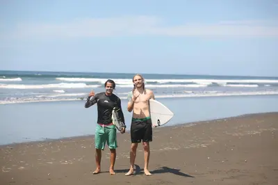 two men standing on the beach with a surfboard at Jaco Surf Beachbungalow in Jacó