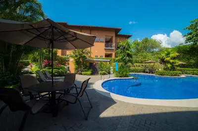 a patio with a table and an umbrella next to a pool at Veranda 1C 3 bdr Golf Course View in Los Suenos in Herradura