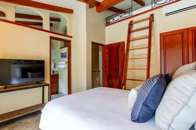a bedroom with a bed with a television and a ladder at Spacious Open-Concept Condo with Stylish Design, Direct Beach Access & Resort-Style Amenities in Playa Flamingo