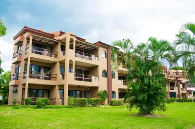 a large building with a palm tree in front of it at Elegant 3BR Beachfront Condo with Spacious Interior, Ocean-View Terrace & Direct Access to Playa Flamingo in Playa Flamingo