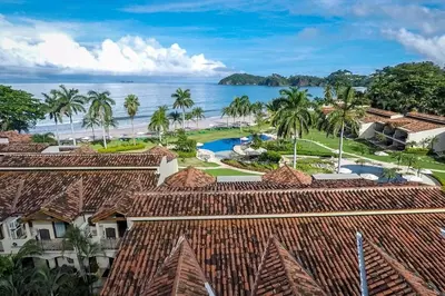 an aerial view of a resort with palm trees and the ocean at Modern Oceanfront Condo with a Chic Coastal Design, Resort-Style Amenities, and Direct Beach Access in Playa Flamingo