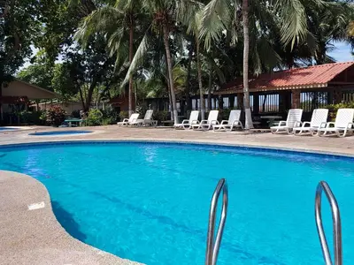 a blue swimming pool with lounge chairs and palm trees at Centro Vacacional Bancosta in Jacó