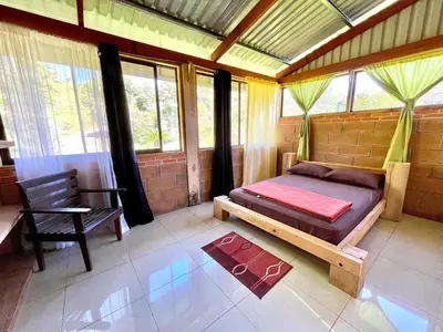 a bedroom with a bed and a chair and windows at Casa Lajas - Casa 1 - Hospedaje, Granja y Turismo Rural in Turrialba