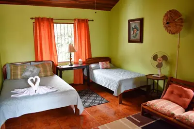 a room with two beds and a chair and a window at Cariari Bed & Breakfast in San José