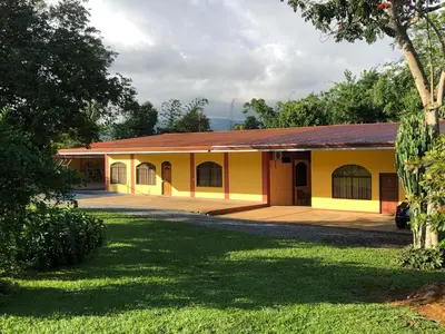 a small yellow building with a grass yard at Hospedaje Adrimaran in Palmares