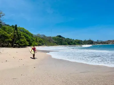 a man standing on a beach holding a surfboard at Tropical House in Nosara- 3 min walk to the beach in Río Seco