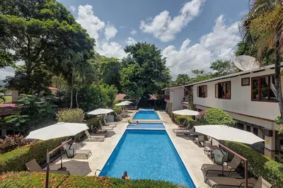 a pool with chairs and umbrellas next to a building at Hotel Mar de Luz in Jacó