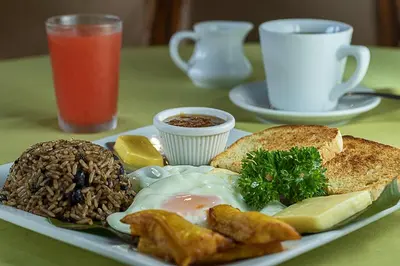 a plate of food with eggs meat and bread on a table at Hotel Mar de Luz in Jacó
