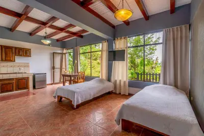 a bedroom with two beds and a kitchen with windows at Ladera Hotel in Turrialba