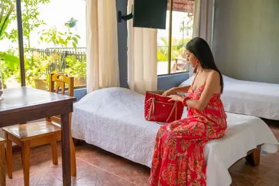 a woman in a red dress sitting on a bed at Ladera Hotel in Turrialba