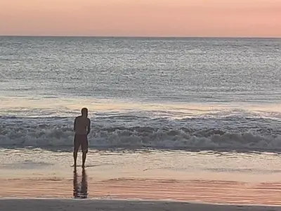 a man standing on the beach looking out at the ocean at Apartotel VILLA ALTA TAMARINDO in Tamarindo