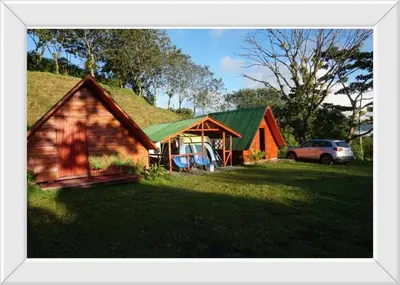 a house with a grass roof with a car parked in front at Sunset Inn Arenal B&B in Fortuna
